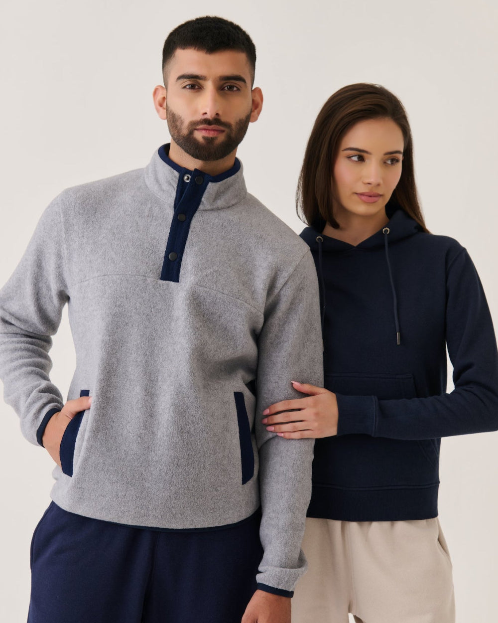 Man and woman wearing matching gray and navy sweaters against a white background
