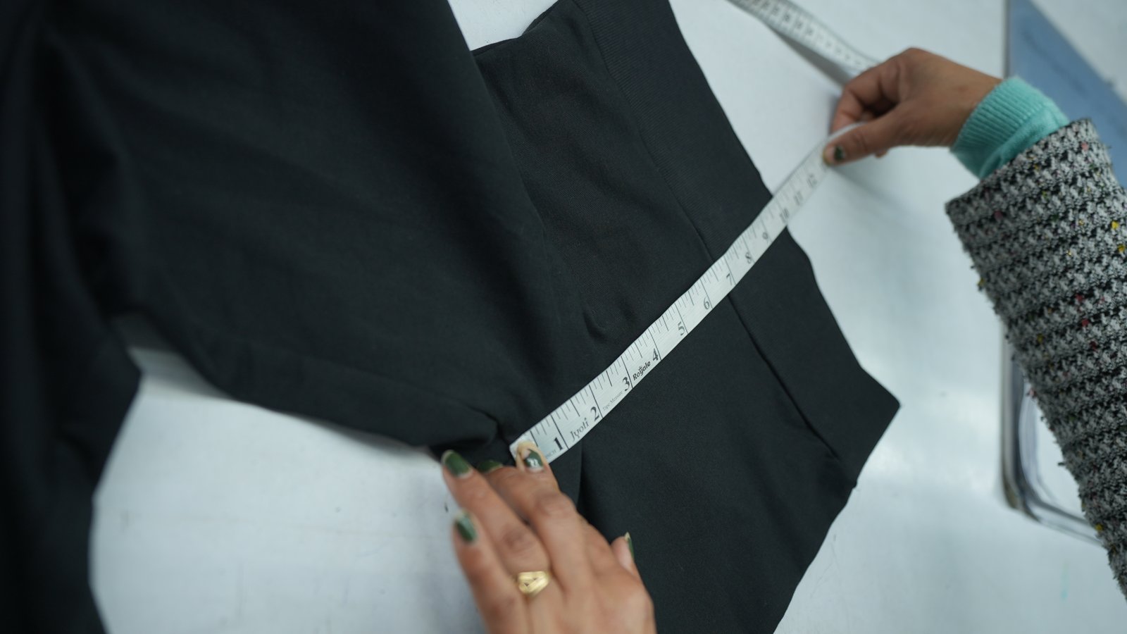Hands measuring a black garment with an inch tape
